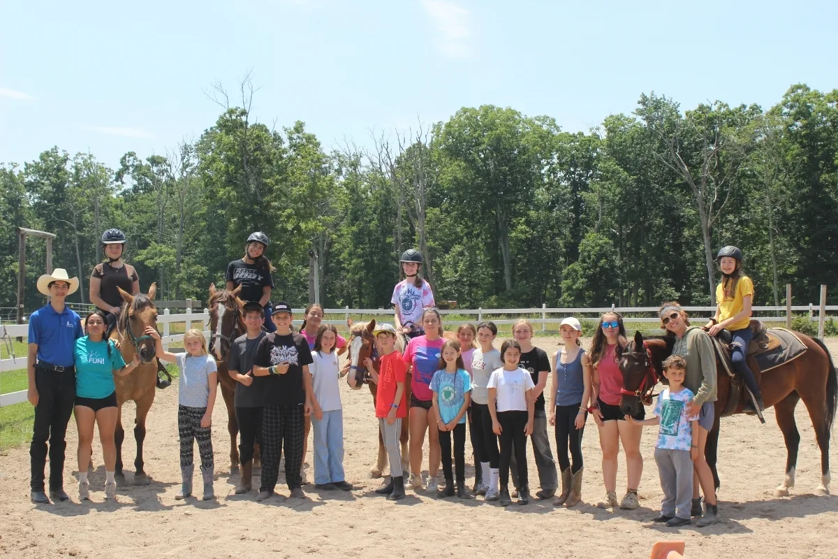 Group of campers and camp staff posing in riding arena with horses at Camp Speers