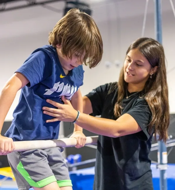 Gymnastics instructor helping youth gymnastics athlete on uneven bar at Haverford Y's Gymnastics Center