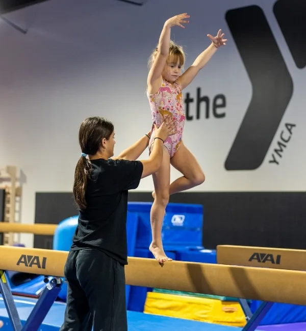 Gymnastics instructor helping youth gymnastics athlete on balance beam