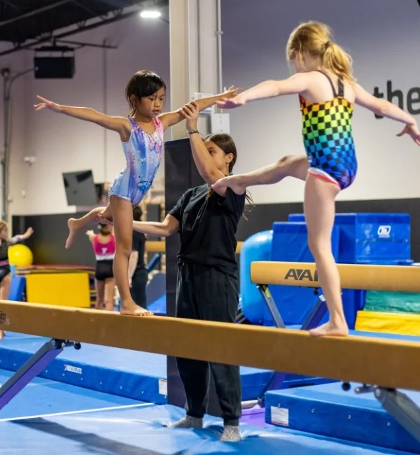 Gymnastics instructor helping youth gymnastics athletes on balance beam