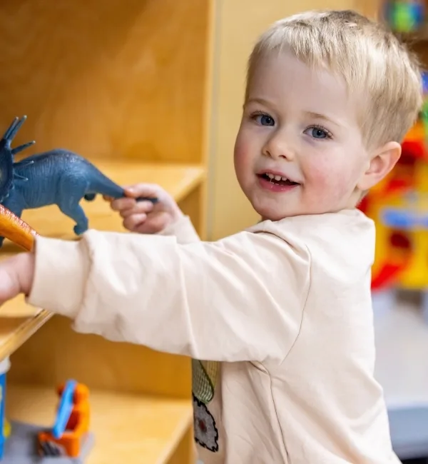 Child playing with toys on a shelf inside a classroom