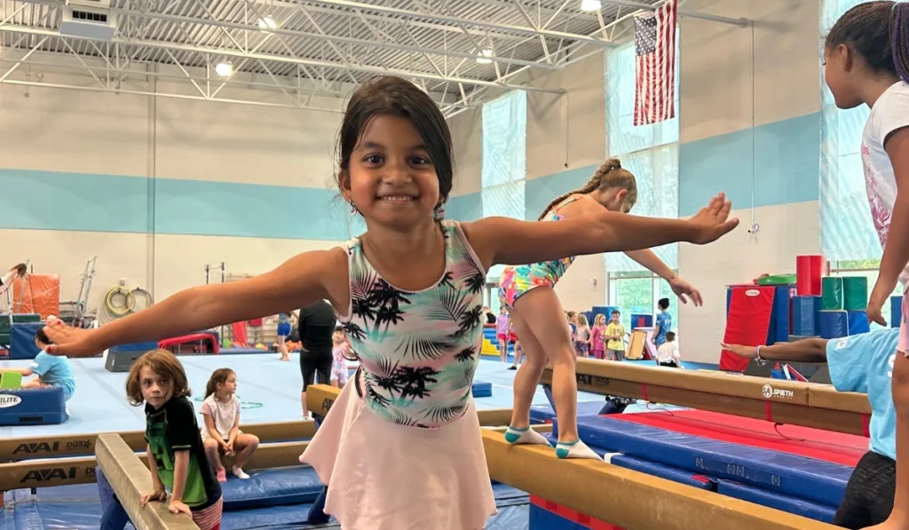 Camper posing on balancing beam at indoor gymnastics facility