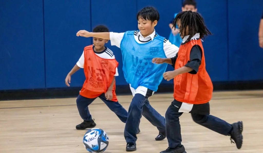 Children playing soccer inside gymnasium
