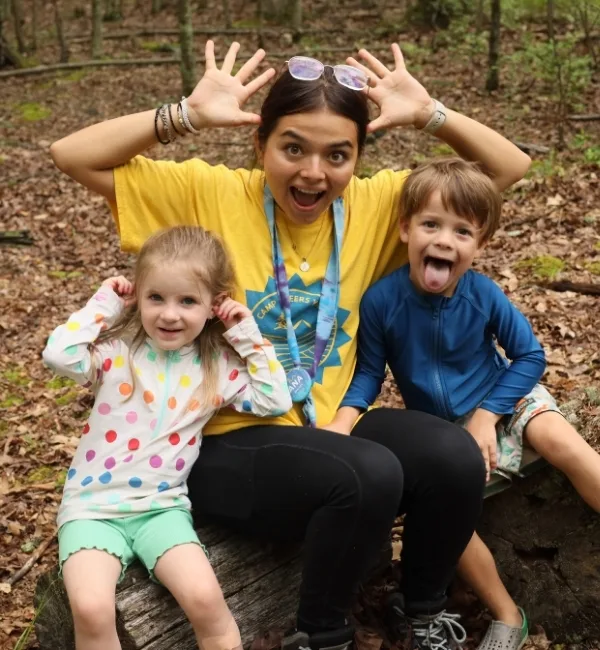 Camp counselor sitting on a log with campers outdoors