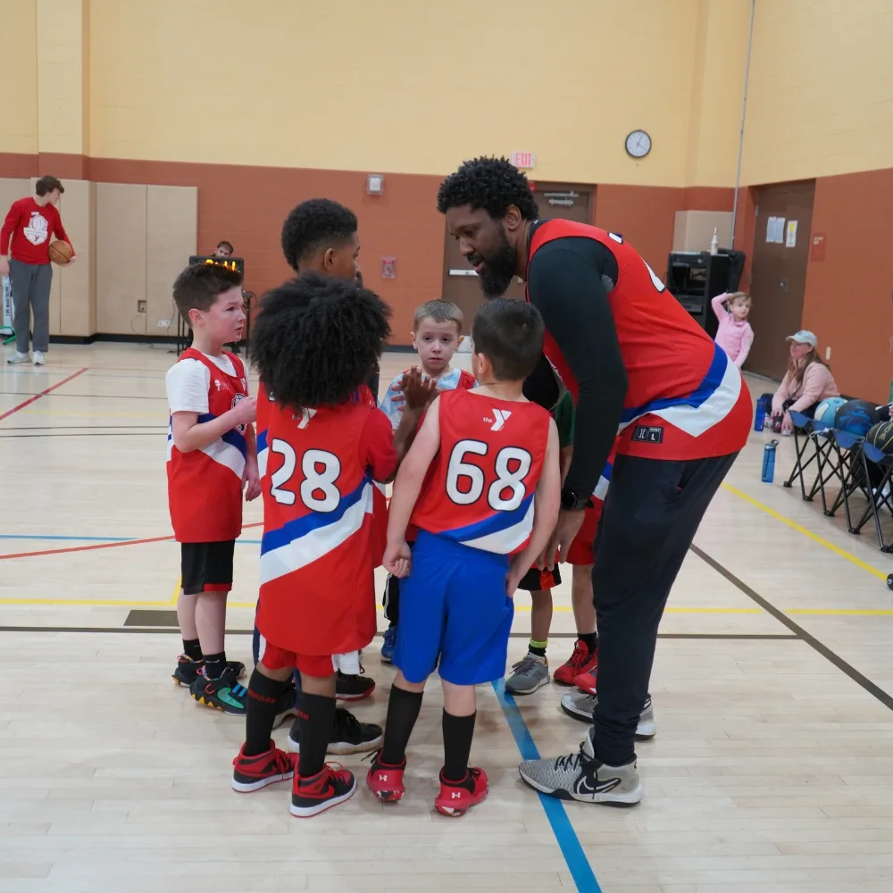 Youth basketball team speaking to coach on indoor basketball court