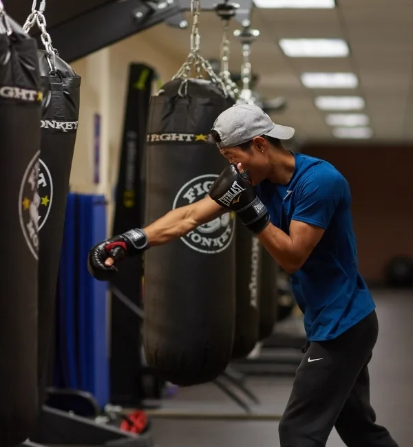 Member boxing with gloves and punching bag inside fitness center