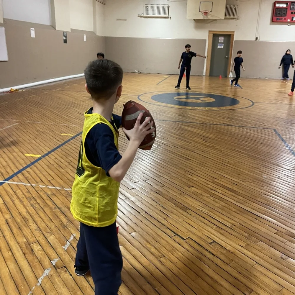 Children playing with football inside indoor gymnasium during Camden Y's CATCH program