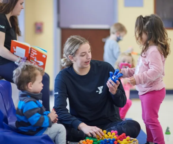 Early learning center staff member and children playing with toys inside classroom