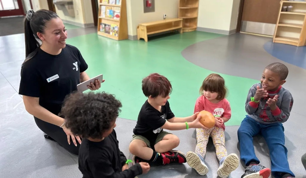 Early Learning Center staff member and children playing hot potato inside classroom