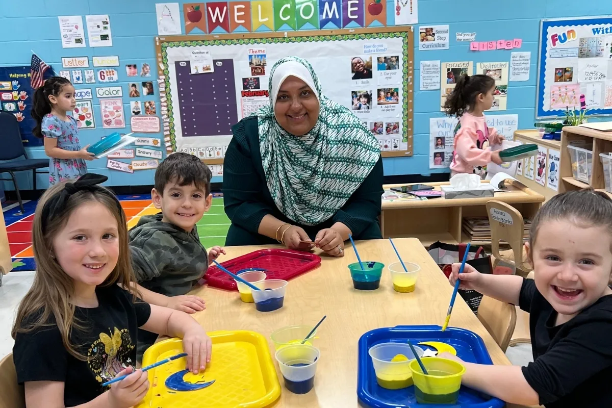 Early learning center staff member and children painting on shapes in a classroom