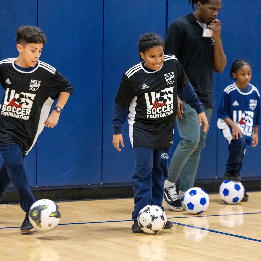 Youth athletes playing soccer inside gymnasium for Soccer for Success clinic