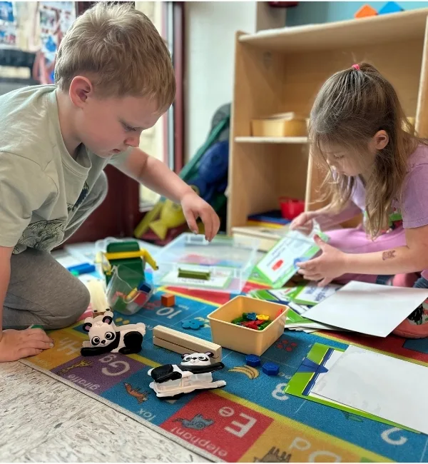Children playing with toys on the ground inside a classroom