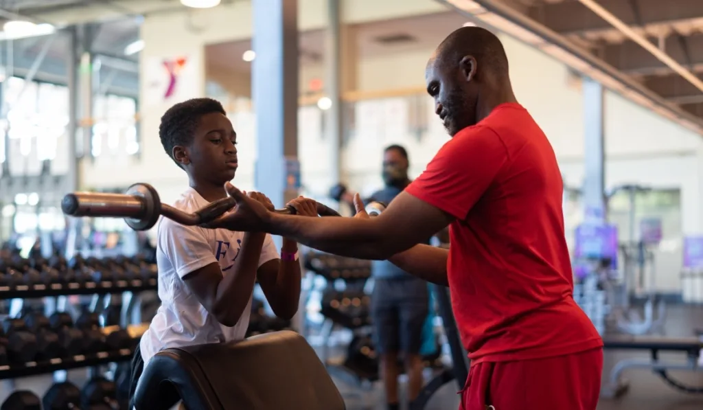Parent helping child use arm curling bar inside fitness studio