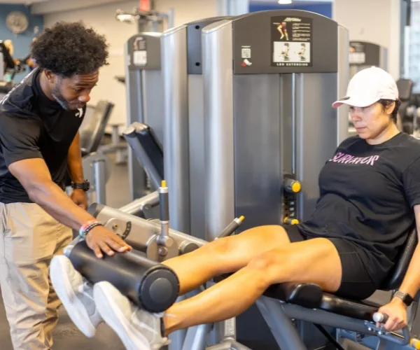 Personal trainer helping a member on a leg lift machine