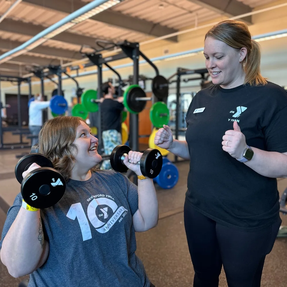 Personal trainer helping a member lift weights inside fitness center