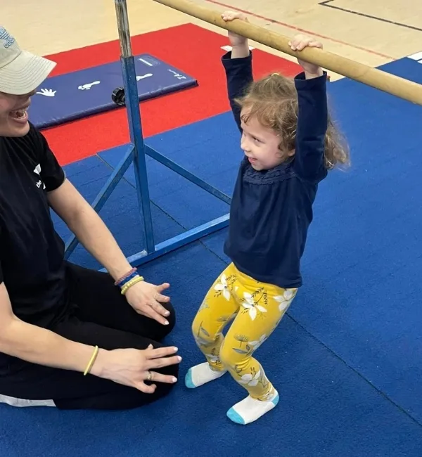 Gymnastics coach and toddler practicing on a high bar inside gymnasium
