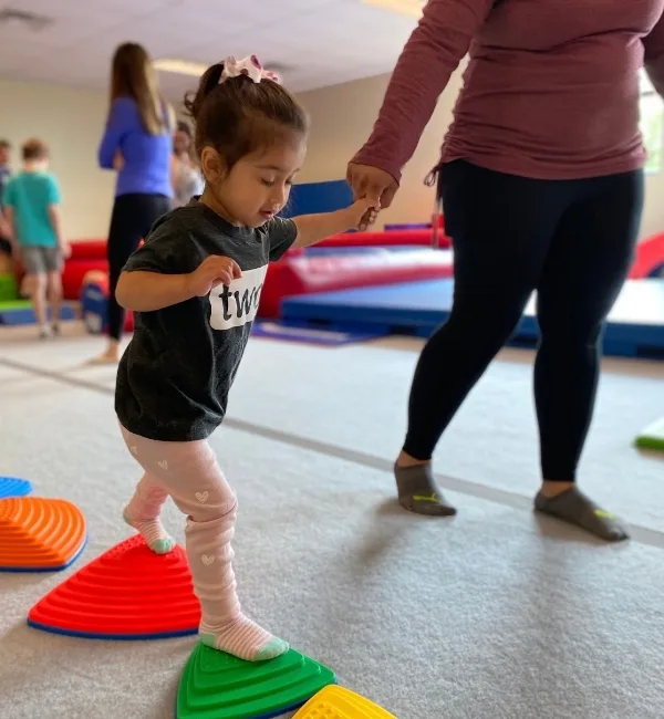Toddler practicing stepping on pads inside a gymnastics studio