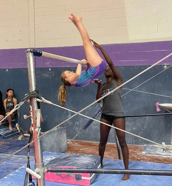 Gymnastics coach helping a child on a high bar inside a gymnastics facility