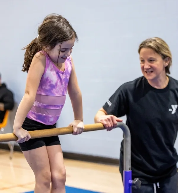 Gymnastics coach helping a child on a high bar inside a gymnasium