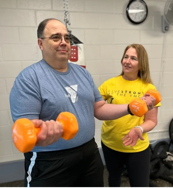 Livestrong personal trainer helping member lift dumbbells