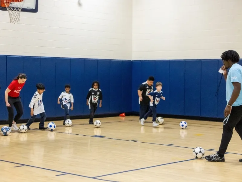 Children playing soccer inside gymnasium during soccer clinic