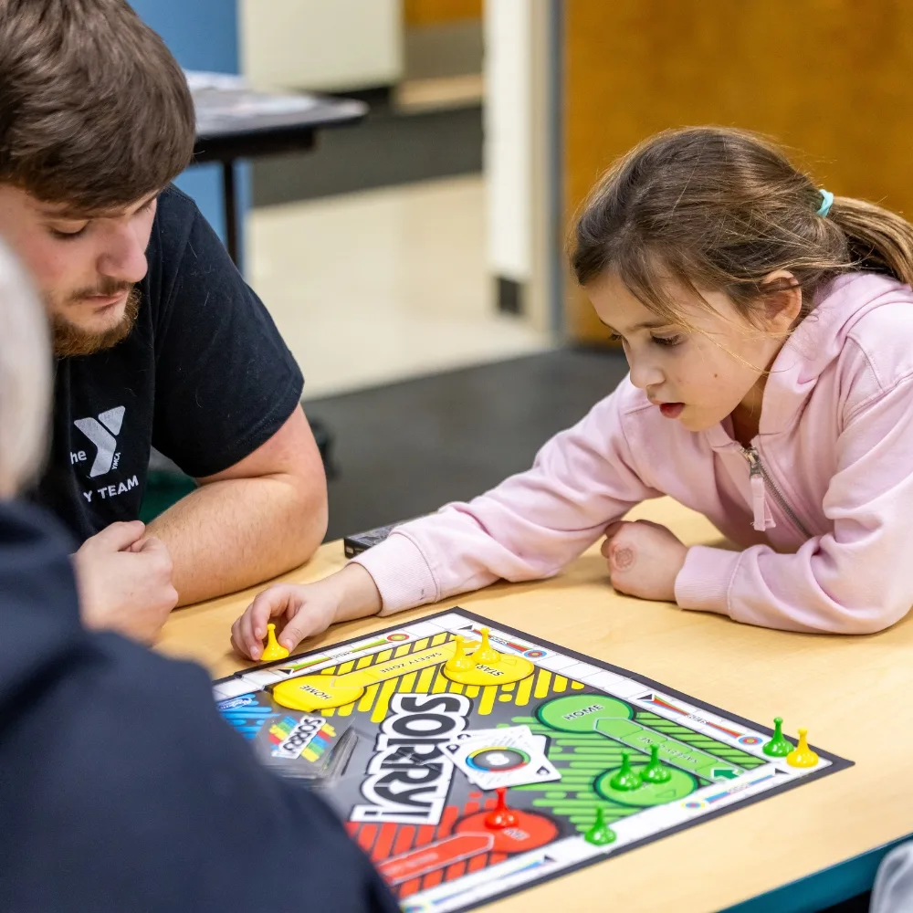 Children playing a boardgame with Y team member inside KidZone area