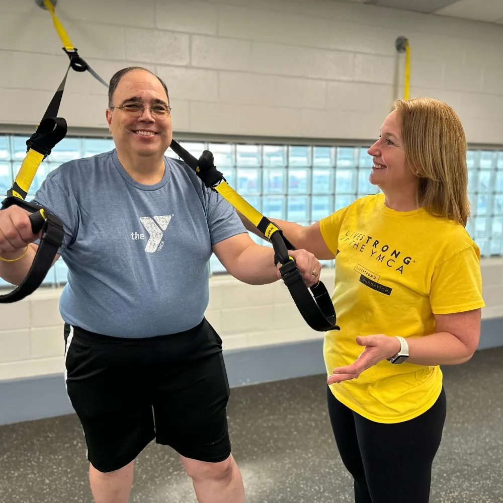 Personal Livestrong trainer helping a member use the TRX equipment inside fitness center