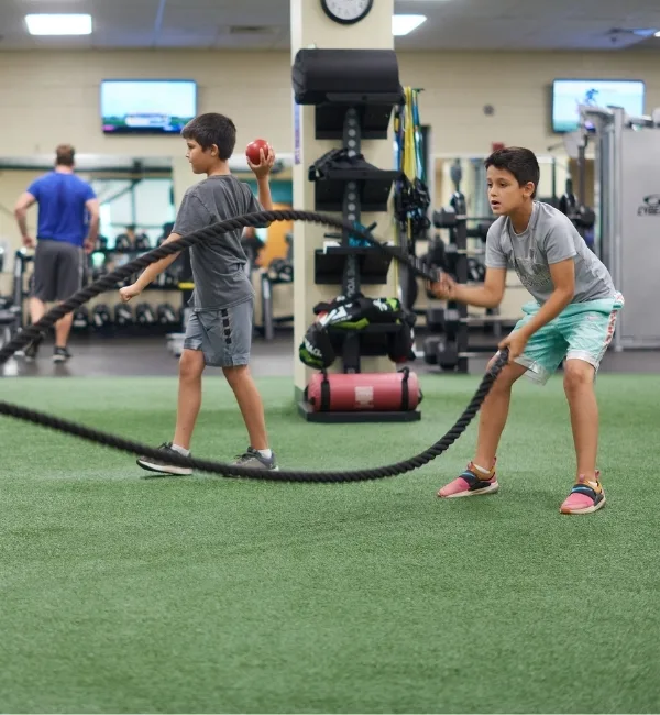 Youth member using exercise ropes on indoor turf area in fitness center