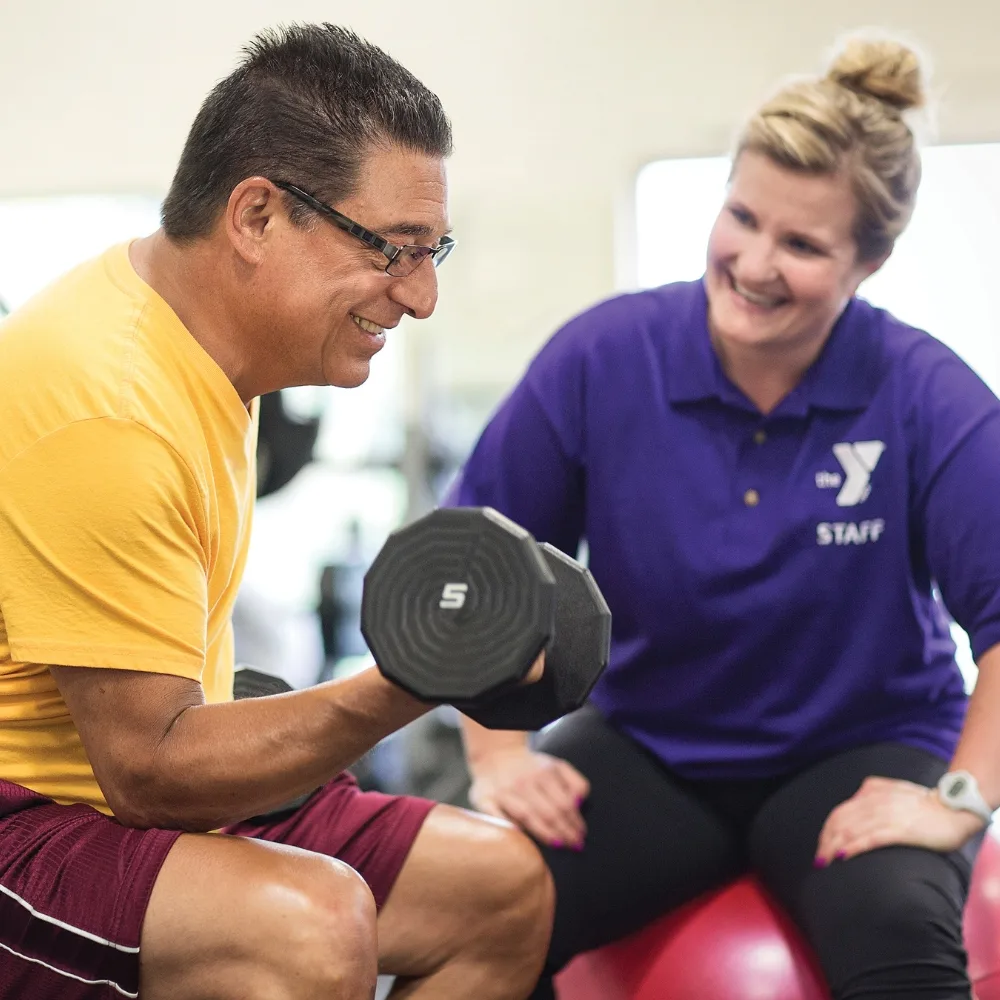 Personal trainer helping member do arm curls with weights inside fitness center