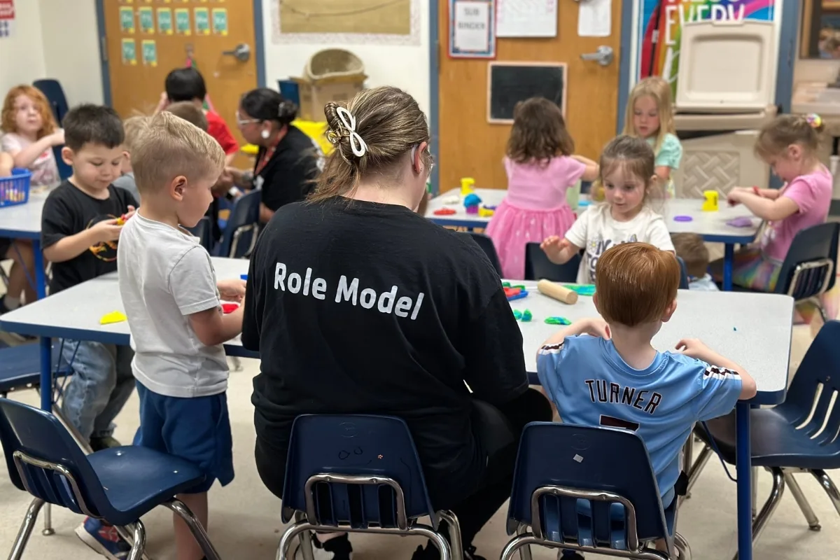 Pre-K staff member helping a group of children play with toys in a classroom