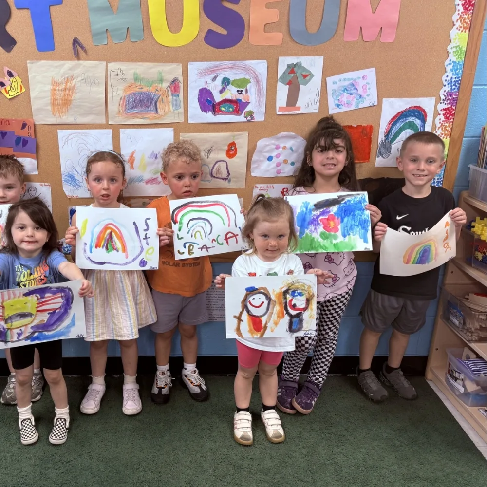 Group of children holding paintings in classroom