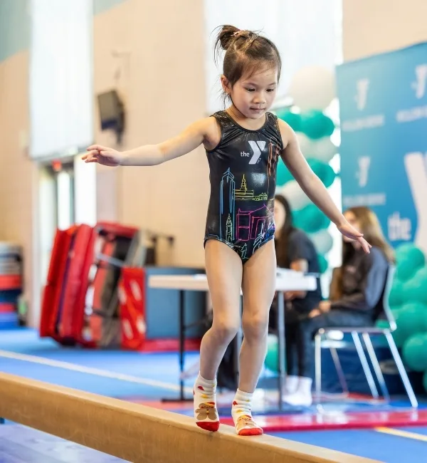 Gymnastics camper on a balance beam at indoor gymnastics facility