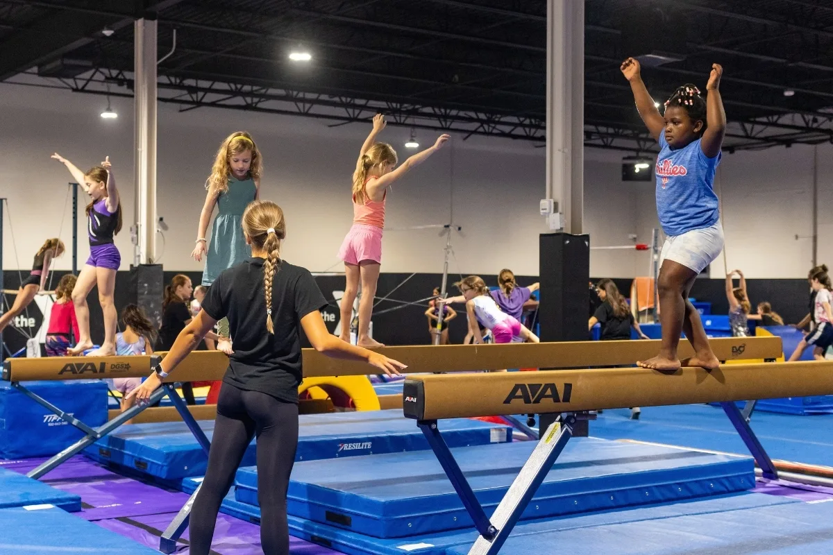 Youth gymnastics campers inside gymnastics facility on balance beams