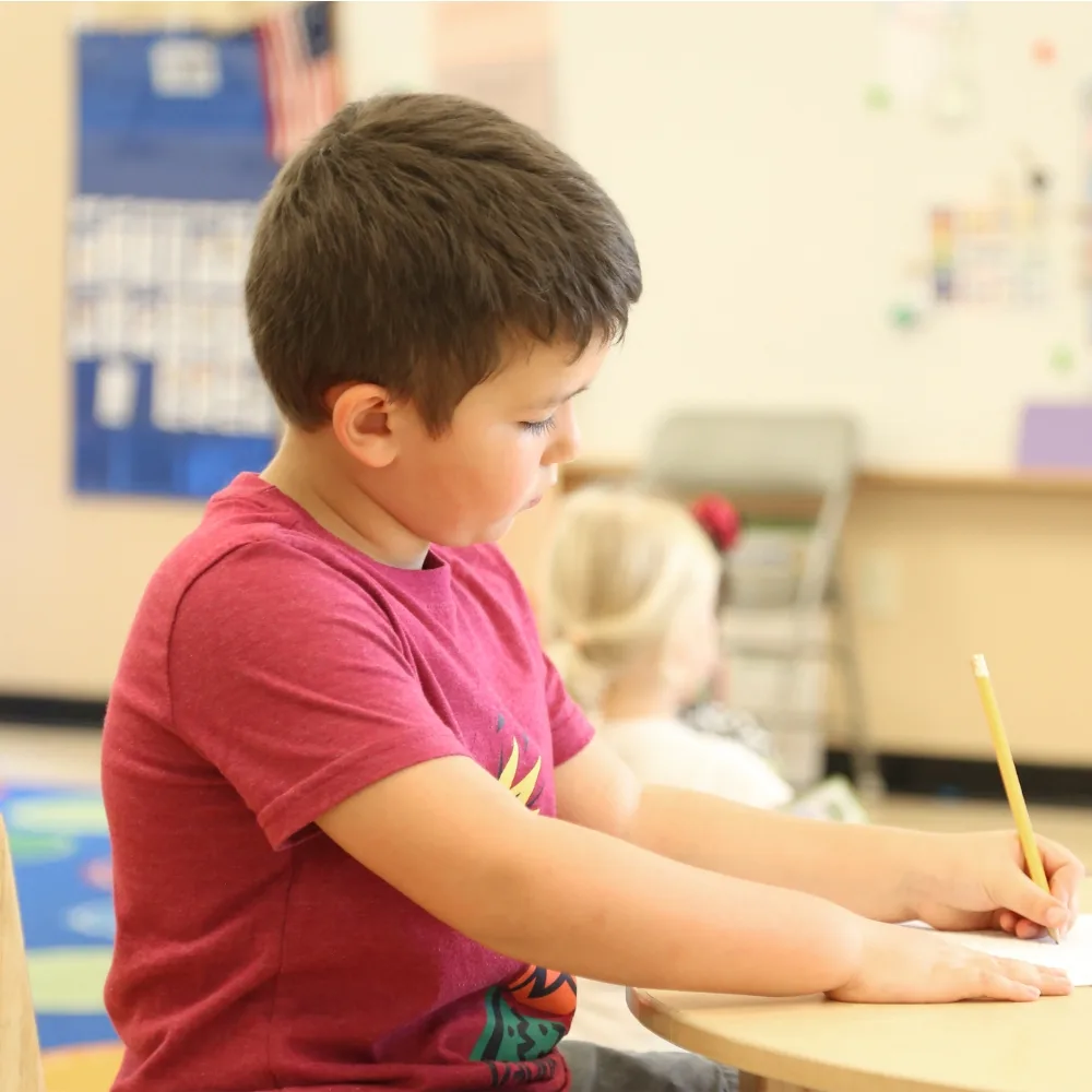 Child writing on paper in classroom