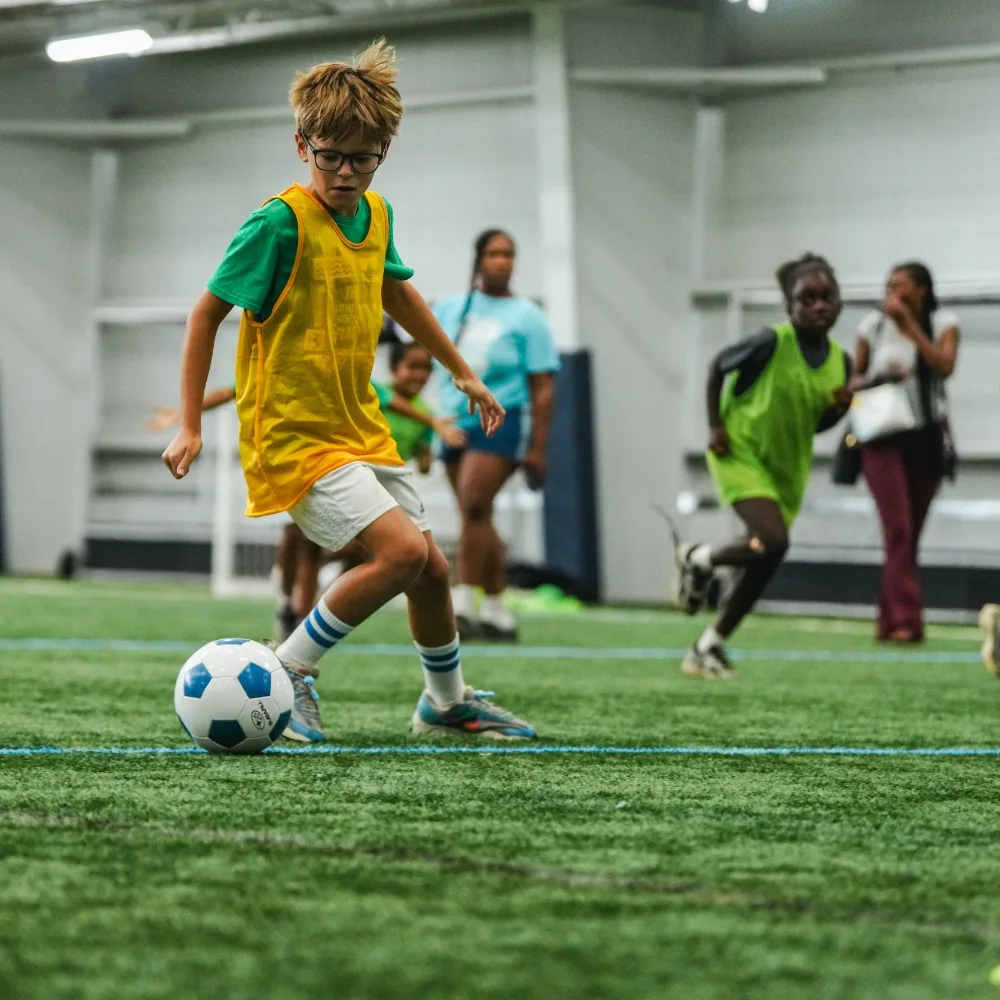 Youth playing soccer on turf inside sports complex