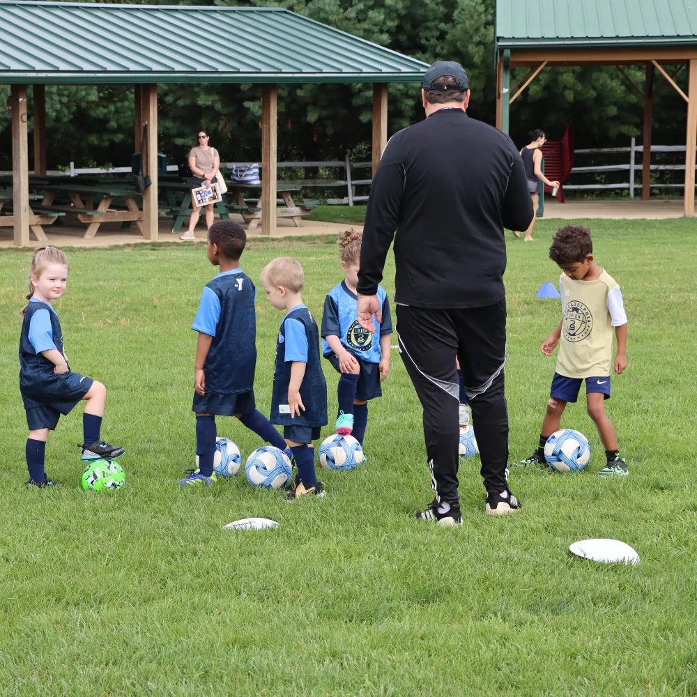 Children and coach practicing soccer on field