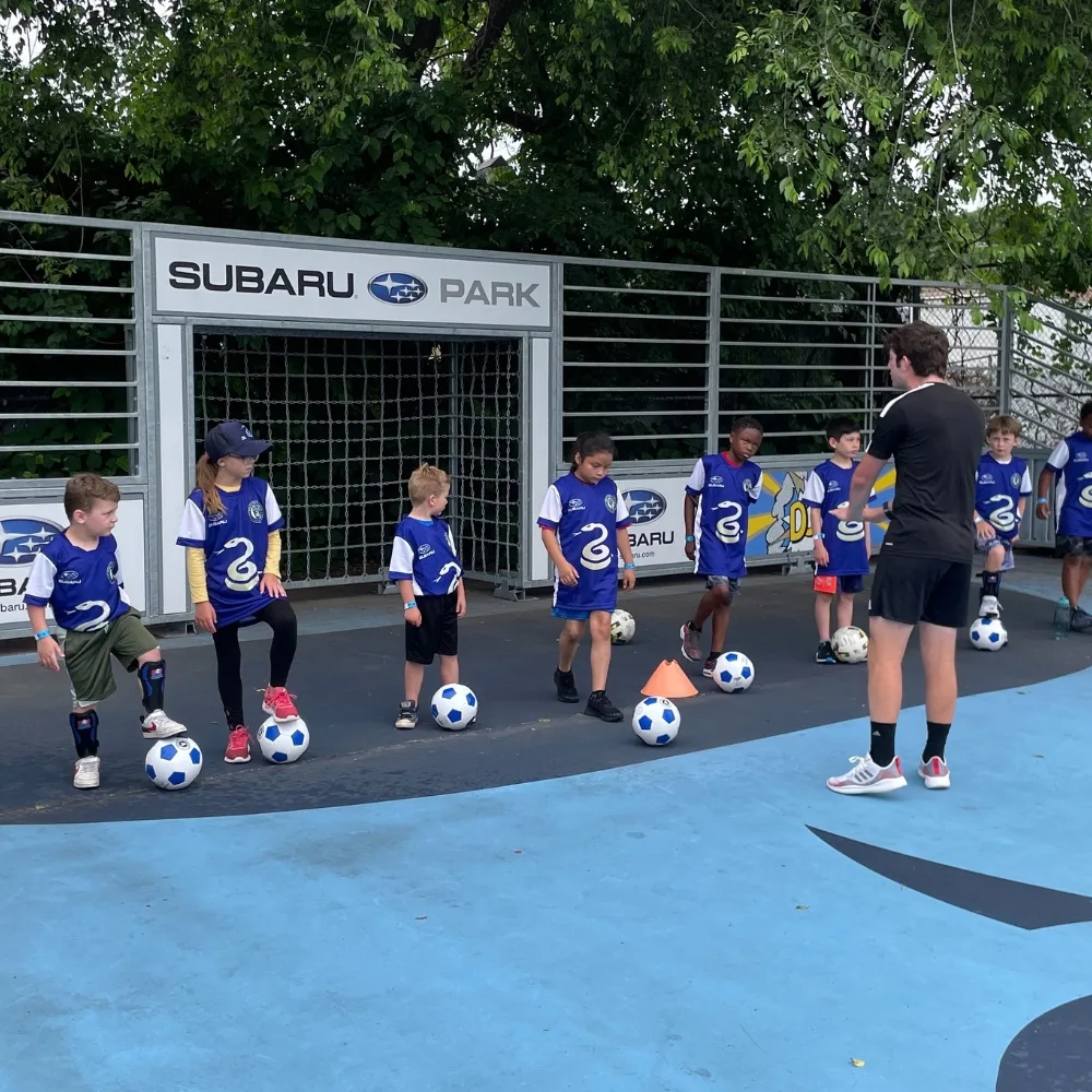 Youth athletes at Soccer for Success sports clinic kicking soccer balls