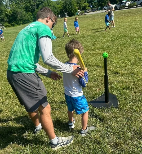 Coach helping child play t-ball on a field