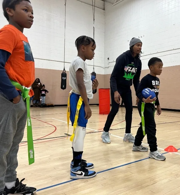 Children practicing flag football with coach on indoor basketball court