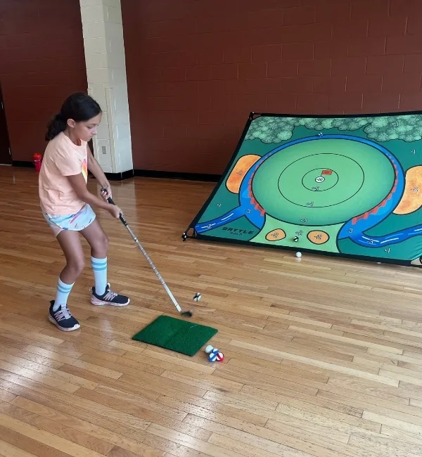 Child practicing golf inside gymnasium