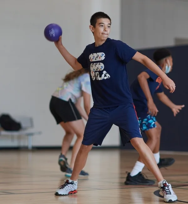Child throwing a ball during dodgeball game inside gymnasium
