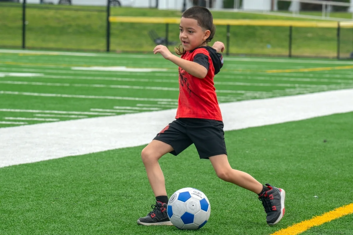 Youth soccer athlete kicking a soccer ball on turf outside