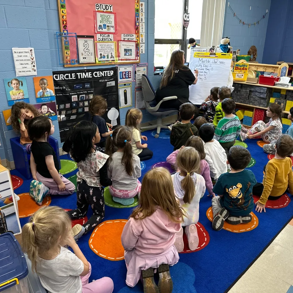Teacher leading lesson to children on carpet inside classroom