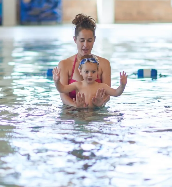 Parent teaching child to swim with swim toys in an indoor pool