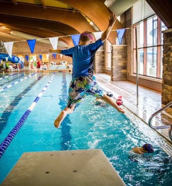 Child jumping off diving board in indoor pool
