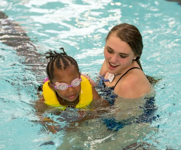 Y swim instructor teaching child to swim inside indoor pool
