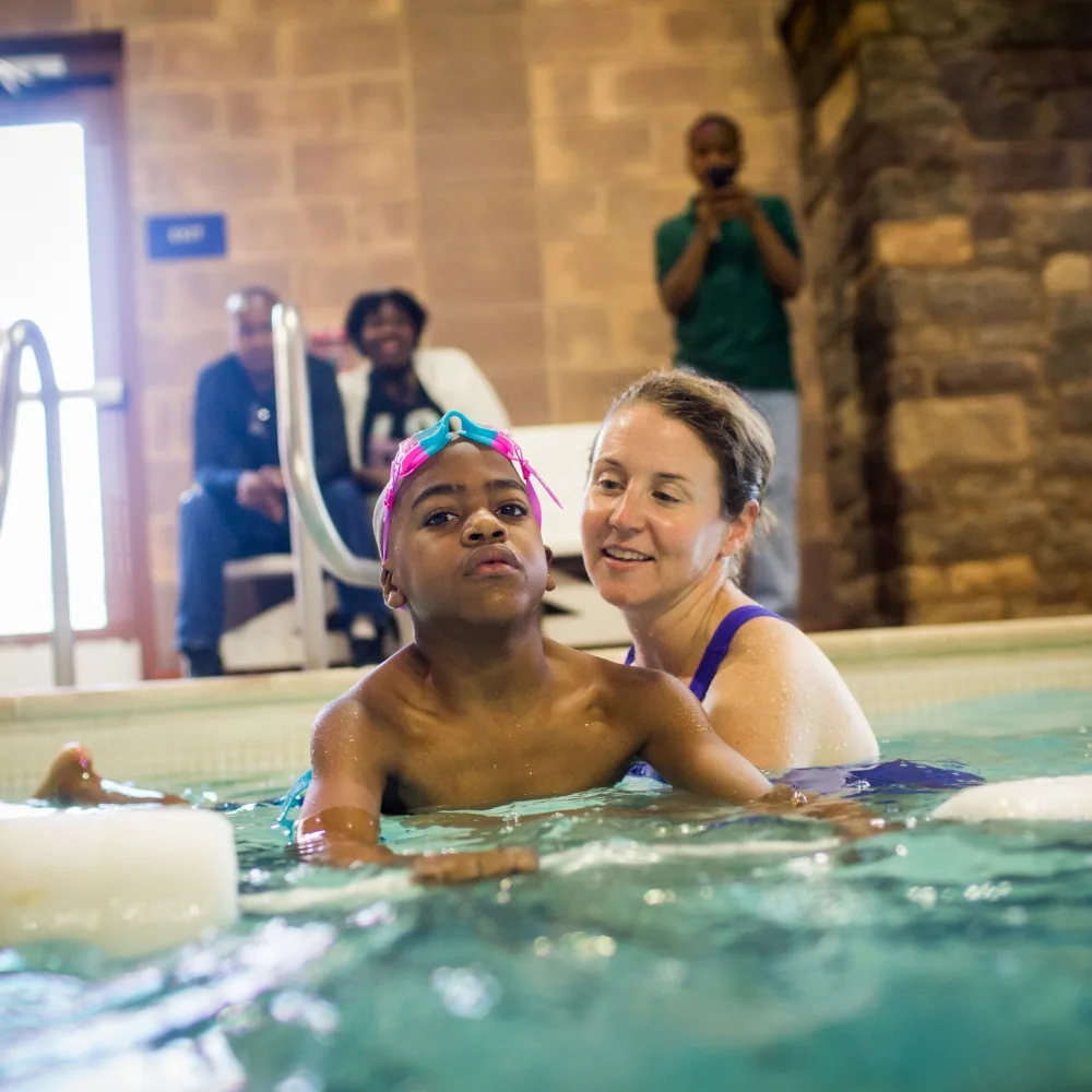 Child learning to swim with swim instructor in an indoor pool