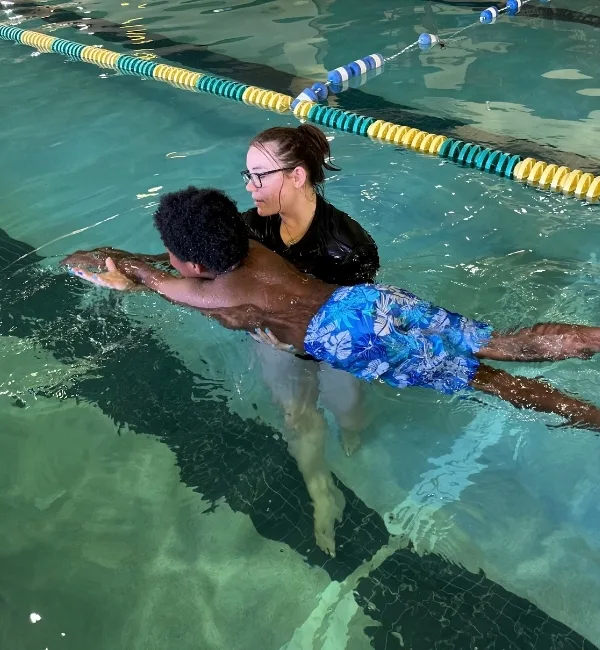 Swim instructor teaching child how to float in indoor pool