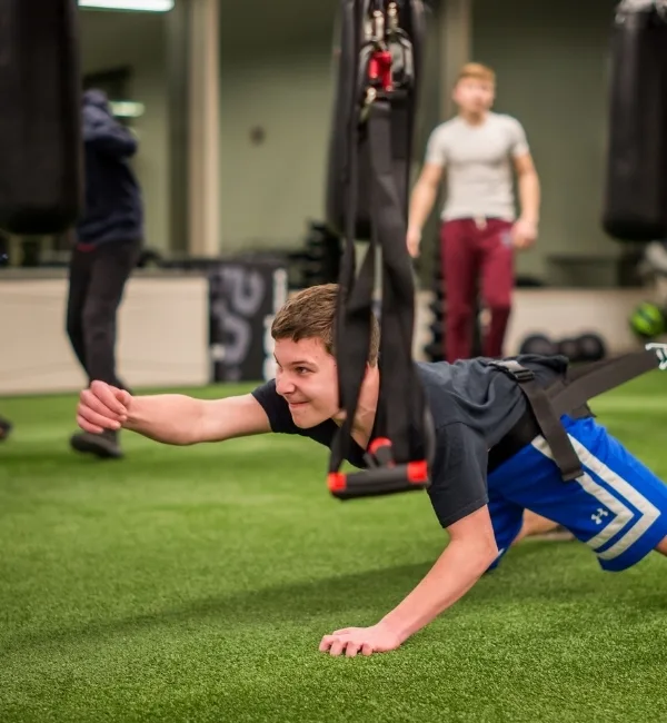 Teen using resistance training equipment on turf area inside a fitness center